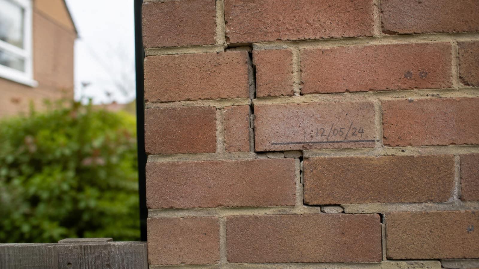 Close-up of a stepped crack in brickwork with a pencilled monitoring date beside it